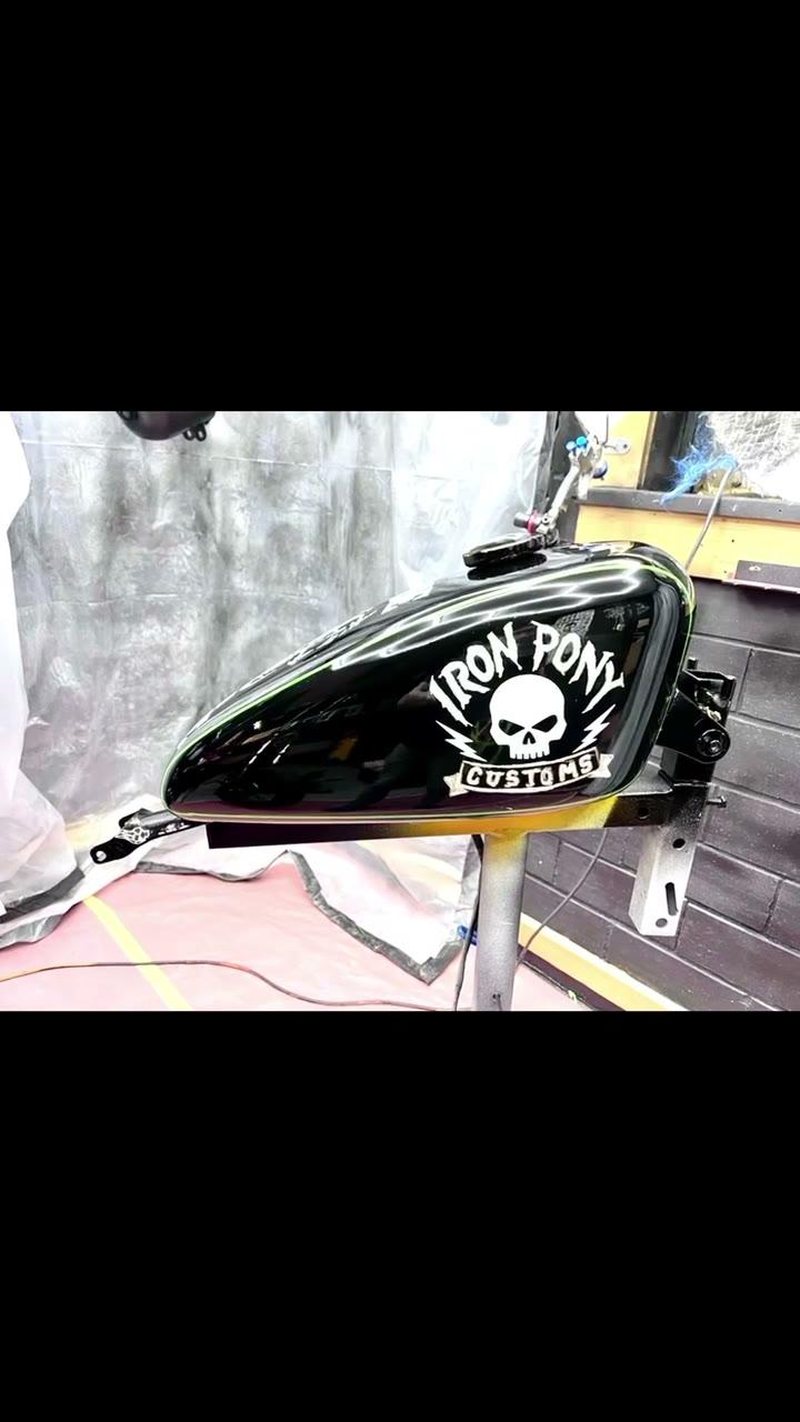 Finished gloss-black Iron Pony Customs tank with the skull logo, turning on the booth stand