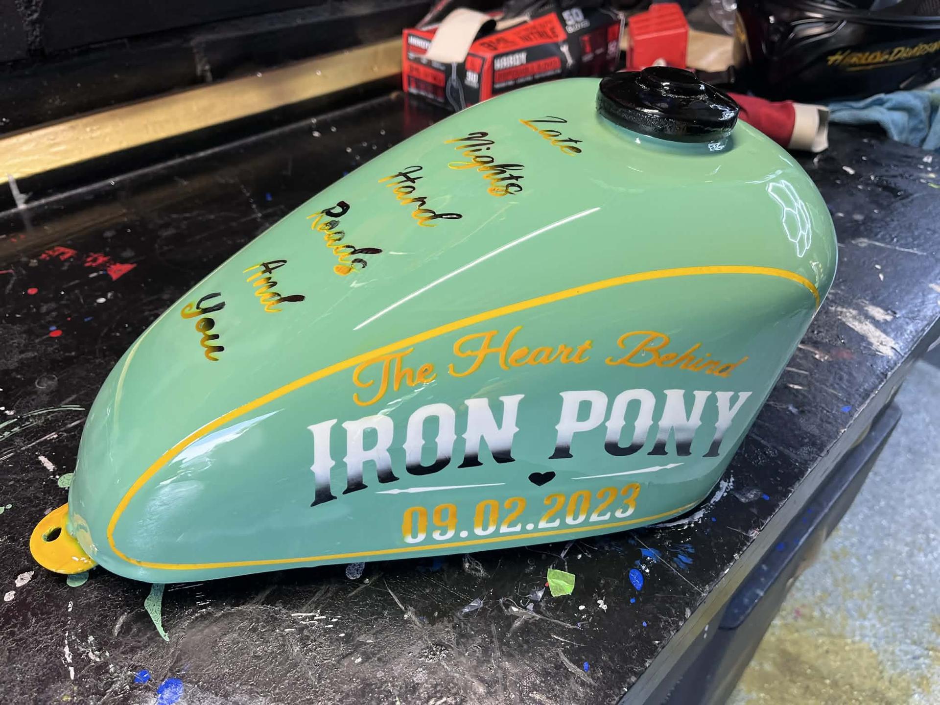 Lime-green custom motorcycle tank with cursive "Feeds" script and the Iron Pony Customs skull logo