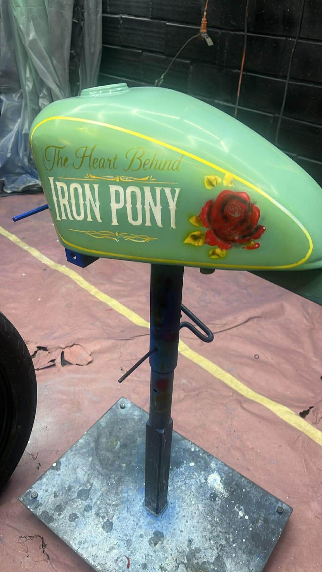 Lime-green Iron Pony Customs tank on a paint stand — skull logo with gold pinstriping